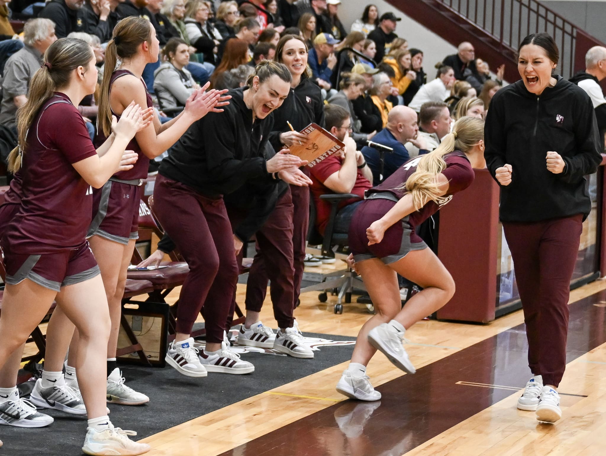 Spearfish Spartans girls basketball bench celebrating a made basket, with players and coaches cheering enthusiastically during a game against the Mitchell Kernels.