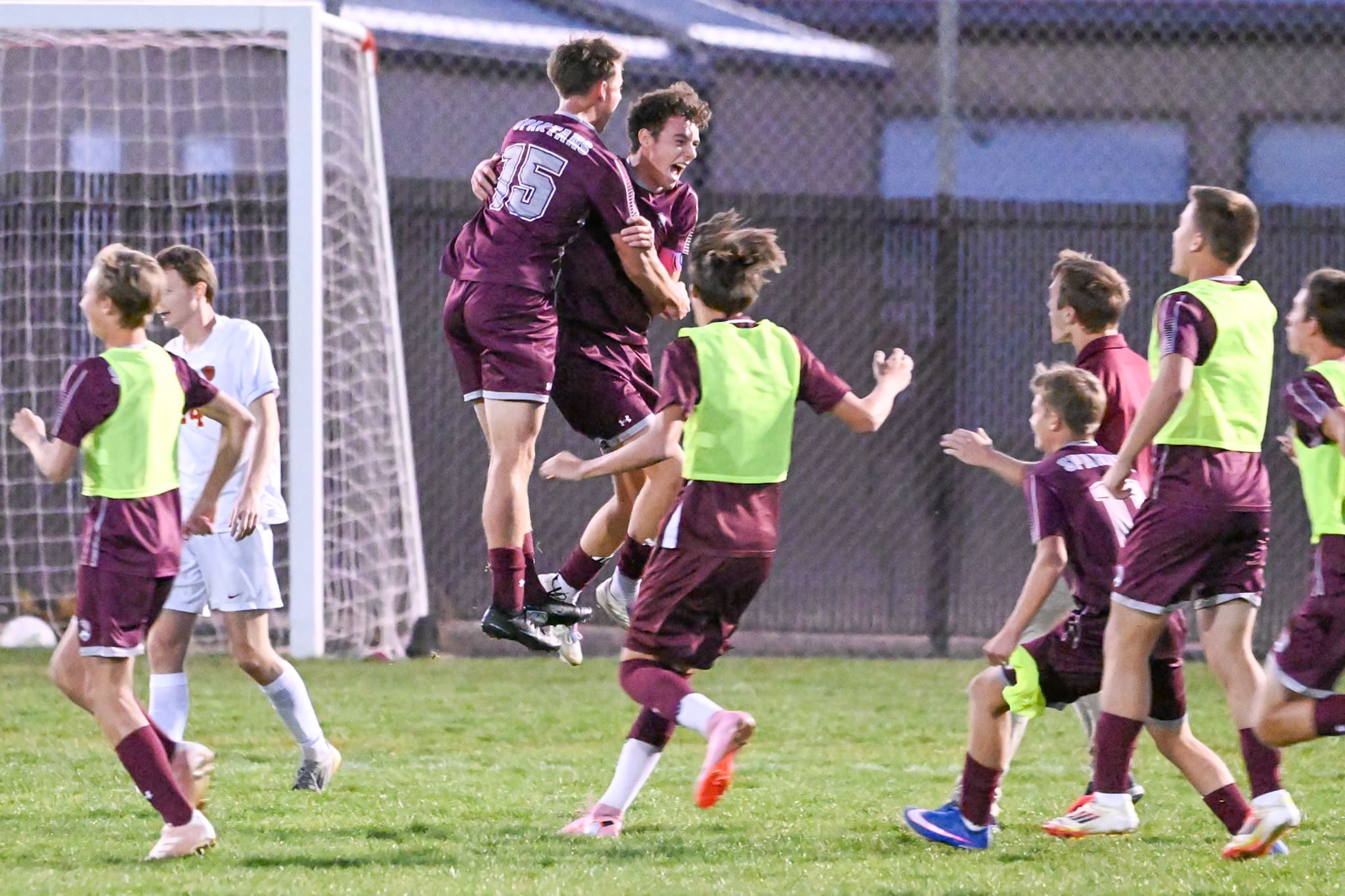 Spearfish boys soccer players in maroon leap and embrace as teammates in green pinnies rush off the bench to celebrate Evan Duncan's late goal against Sioux Falls Roosevelt.